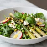 Colorful spring salad recipe with fresh greens, asparagus, peas, radishes, and lemon vinaigrette in a white bowl
