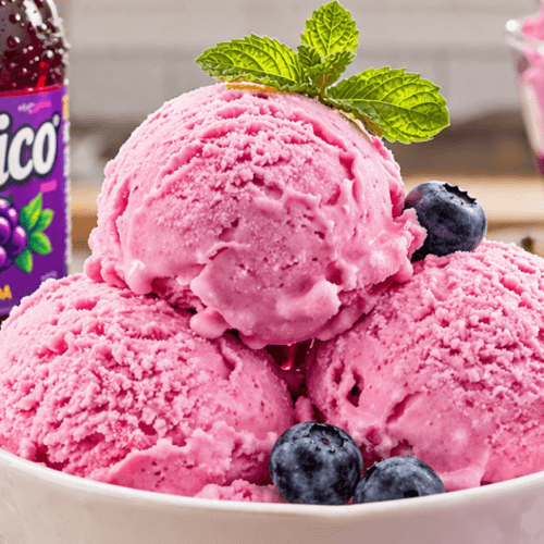 Bowl of bright pink Grapico ice cream scoops with blueberries and mint, styled beside a bottle of Grapico grape soda.