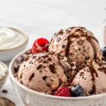 High protein ice cream scooped into a bowl with chocolate drizzle, berries, cottage cheese, and Greek yogurt.