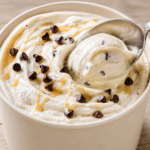 Ninja Creami Cottage Cheese Ice Cream with chocolate chips and caramel drizzle scooped from a creamy pint.