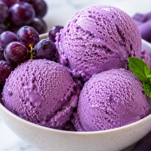 Grape ice cream recipe served as creamy purple scoops in a bowl with fresh grapes and mint