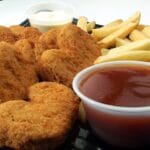 A basket of golden crispy chicken nuggets served with french fries and dipping sauce
