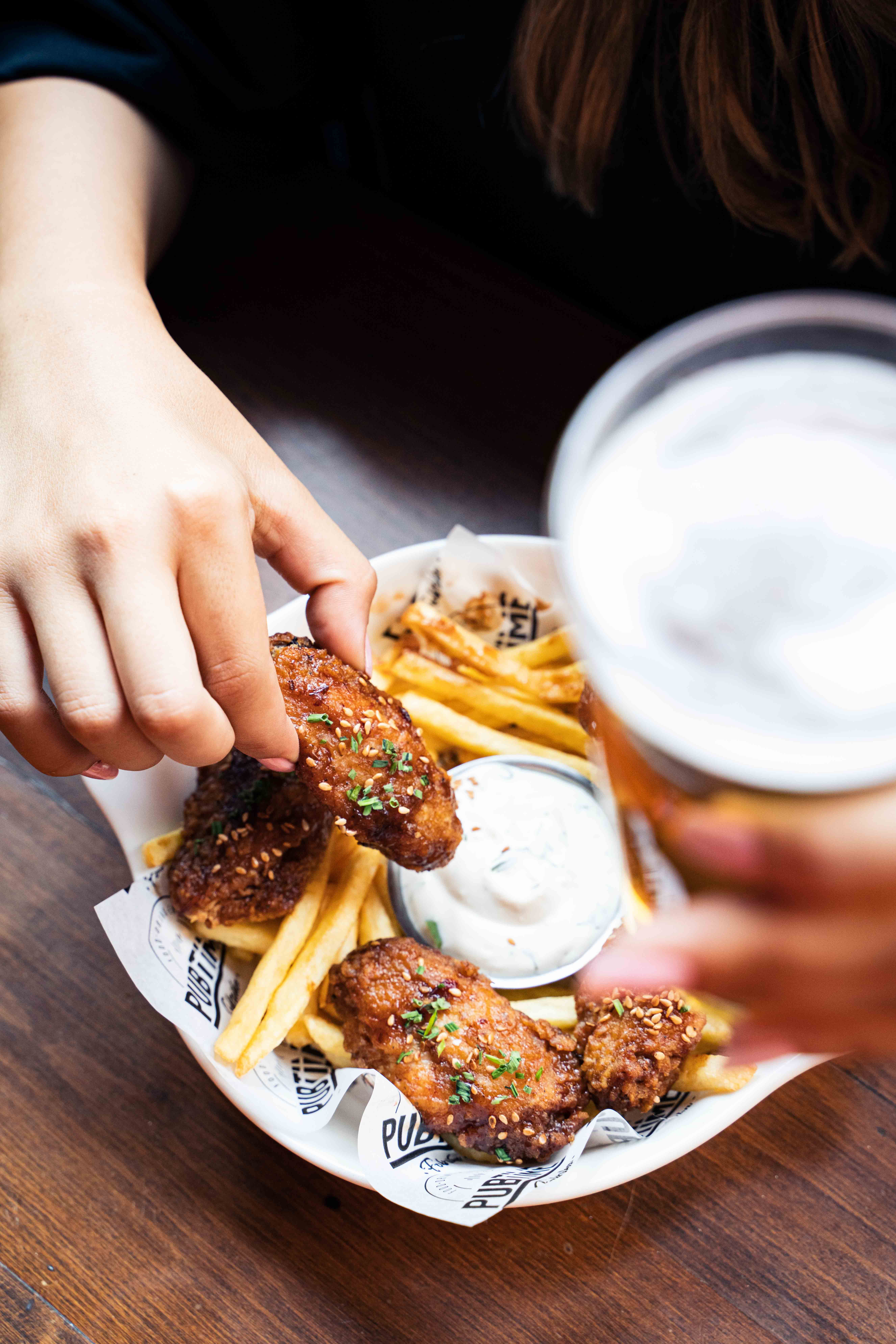 Close-up of hands holding crispy chicken nuggets and fries with creamy dipping sauce